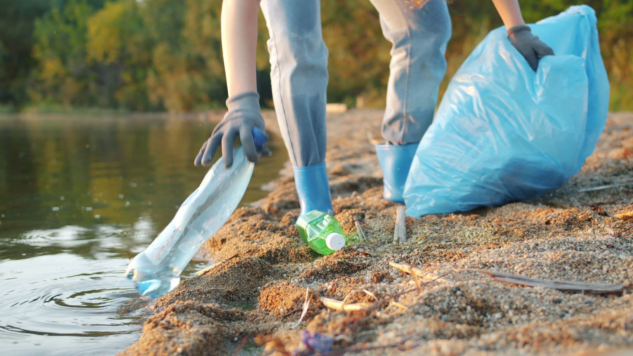 Relawan bersarung tangan memungut botol plastik dari tepi air